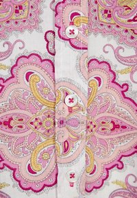Tessuto bianco con intricati motivi paisley in rosa, giallo e viola, con tre bottoni bianchi in filo rosa sulla placca della camicia.