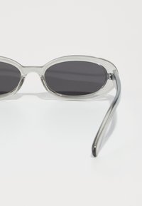 Gafas de sol de acetato transparente con lentes oscuros, de forma ovalada y con brazos suaves y redondeados. Destacan por su diseño minimalista y su textura ligera.