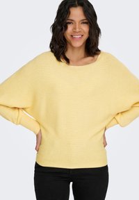 Geel geribd trui met een brede halslijn en vleermuismouwen. De stof heeft een gladde textuur met subtiele horizontale strepen.