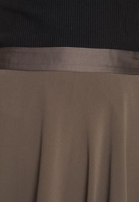 Zone de la taille d'un vêtement montrant un haut noir côtelé rentré dans une jupe taupe lisse avec une large ceinture.