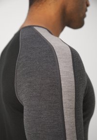 Długa koszula z wełny merino, ciemnoszara z jasnoszarymi paskami na ramionach, dopasowany krój, gładka tekstura, okrągły dekolt i płaskie szwy.