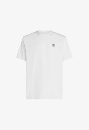 Valkoinen puuvillainen T-paita pyöreällä kaula-aukolla, lyhyillä hihoilla ja pienellä logopläkki vasemmassa rinnassa. Sileä tekstuuri ja klassinen istuvuus.