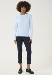 Hellblauer, gestrickter Pullover mit gewelltem Halsauschnitt, kombiniert mit dunkelblauen, enganliegenden Hosen und schwarzen Slippern. Ganze Strukturmuster.