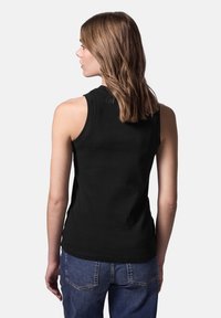 Camiseta sin mangas negra de algodón, con escote redondeado. Combinada con jeans de mezclilla azules, mostrando la vista trasera.