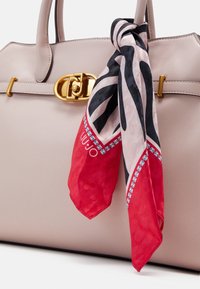 Sac à main en cuir beige avec fermeture à cliquet dorée et un foulard à motifs rouges, noirs et blancs attaché à une anse.