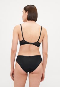 Zwart lingerieset bestaande uit een beha met verstelbare bandjes en een haaksluiting, gecombineerd met hoge slipjes met een golvende rand.