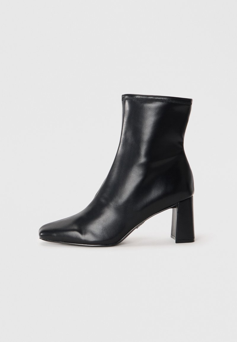Botte de cheville en cuir noir avec un bout pointu et un talon carré structuré. Texture lisse avec un design épuré et minimaliste.
