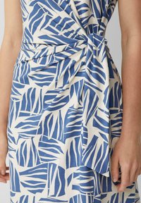 Niebieska i biała sukienka w wzory z motywem liści, z węzłem w talii i miękką, teksturowaną tkaniną.