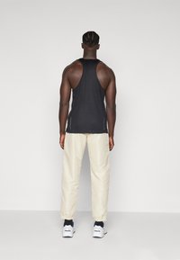 Svart tank topp med racerback-design, kombinert med kremfargede bukser med elastiske ankler og hvite sneakers med marineblå detaljer.