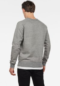 Sudadera gris de tela suave, con cuello redondo, puños y dobladillo acanalados, y un diseño simple sin gráficos ni patrones.