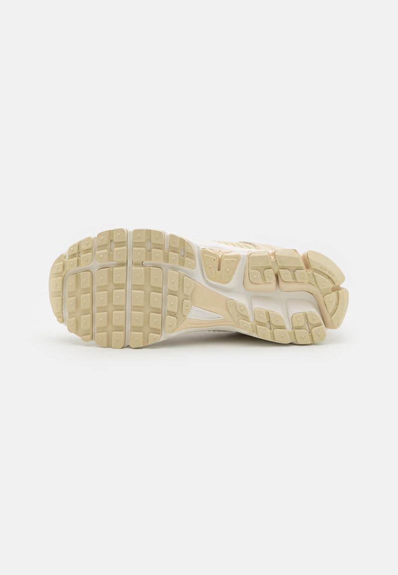 Suela de zapatilla deportiva beige con dibujo en relieve, que presenta componentes de goma texturizada y ranuras distintivas para agarre y soporte.