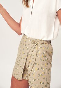 Lichtgewicht wit blouse gecombineerd met beige korte broek met een bloemenpatroon in geel en wit, met een gestrikt taille detail en een relaxte pasvorm.