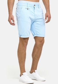 Pantalones cortos de algodón azul claro con puños enrollados, que cuentan con dos bolsillos laterales, cintura con botón y sutiles detalles de costura.