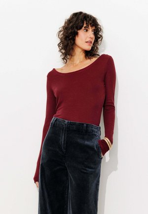 Haut bordeaux à manches longues avec un col en dentelle, associé à un pantalon en velours côtelé bleu marine taille haute, mettant en valeur une texture douce et une coupe décontractée.