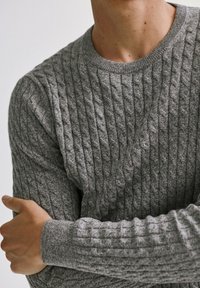 Pull gris en tricot avec un motif côtelé texturé, col rond et manches longues. Le tissu semble doux et légèrement duveteux.