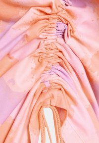 Sběrná tkanina v odstínech růžové a levandulové, s texturovaným povrchem jemnými vzory a elastickým stahovacím detailem.