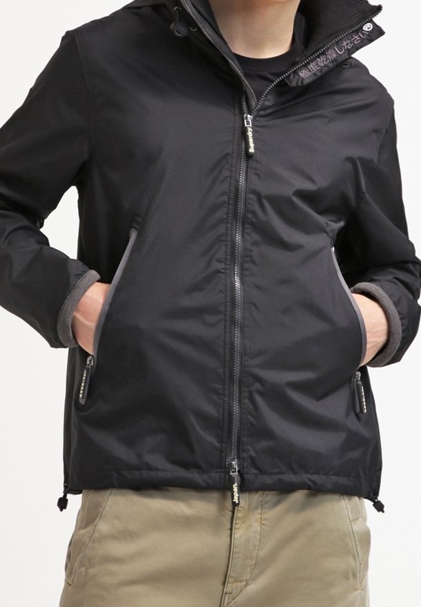 Czarna wodoodporna kurtka z zamkiem błyskawicznym z przodu, regulowanym kapturem oraz kieszeniami wyściełanymi szarą polarem. Posiada gładką, matową fakturę.