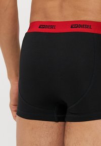 Schwarze Baumwoll-Boxershorts mit einem roten elastischen Taillenbund, auf dem das Logo "DIESEL" zu sehen ist. Glatte Textur mit figurbetontem Schnitt und kontrastierenden Nähten.