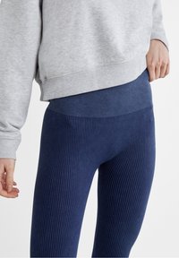 Leggings de canalé en color azul marino con una cinturilla alta, combinados con un sudadera gris claro. Presentan un tejido suave y un patrón texturizado.