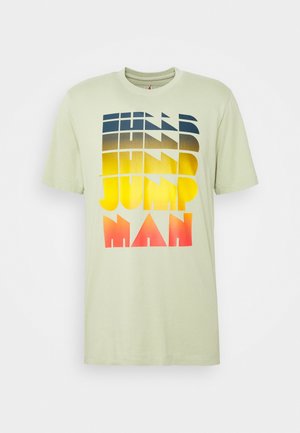 T-shirt en coton vert clair avec un design de texte en dégradé bleu marine, jaune et rouge. Manches courtes et col rond classique.
