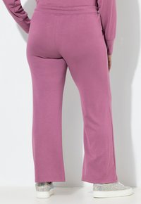 Fialové, volně střižené tepláky s hladkou texturou, vybavené širokým střihem nohavic. V páru s lesklými stříbrnými teniskami.