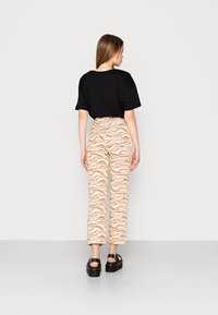 Camiseta oversized preta combinada com calças de cintura alta em zebra nas cores bege e castanho. O visual é finalizado com sandálias chunky pretas.