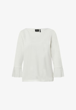 Top à manches longues blanc avec un col bateau et des poignets plissés évasés. Texture de tissu lisse ; design minimaliste. Étiquette de marque visible au niveau du col.