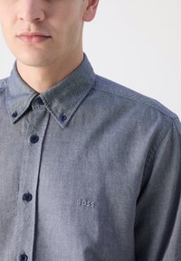 Button-up shirt in dark blue denim with a structured collar, contrasting navy buttons, and subtle "BOSS" embroidery on the chest.
