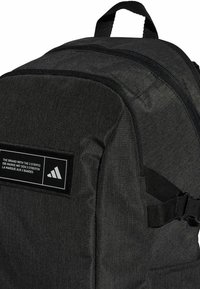 Mochila de tela negra con superficie texturizada, que cuenta con un parche con logo, cremalleras, correas ajustables y un asa en la parte superior para llevar.