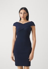 Vestido de canalé azul marino con diseño de hombros descubiertos y una silueta ajustada, que presenta un detalle entrelazado en el cuerpo. Textura suave.