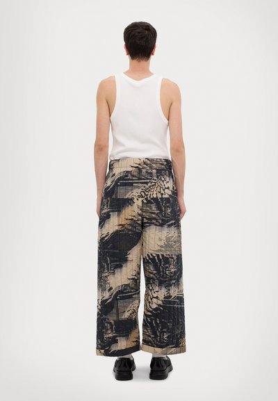 Loose-fit, patterned pants in beige and black. Features a textured design with wide legs and a high waist. Paired with a white tank top.