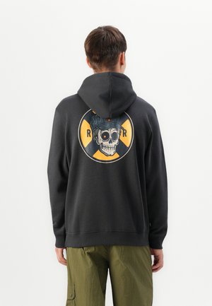 Zwarte hoodie met een grafische print van een schedel die een pet draagt, weergegeven op de achterkant binnen een cirkelontwerp in geel en zwart.