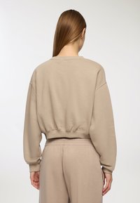 Felpa beige accorciata con orlo a coste, spalle basse e maniche lunghe, abbinata a pantaloni tuta beige coordinati. Texture del tessuto morbida.