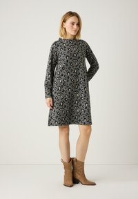 Graues Langarmkleid mit Leopardenmuster, mit hohem Ausschnitt und lockerer Passform. Getragen mit tanfarbigen Wildleder-Ankle-Boots.