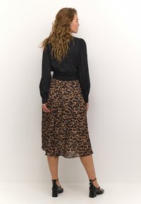 Crna bluzica s dugim rukavima, plisirana suknja s leopard uzorkom u smeškastim i crnim nijansama, uparen sa crnim salonkama, prikazano iz pozadine.