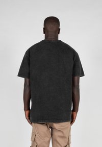 Camiseta negra de corte oversize hecha de algodón, con mangas cortas, cuello redondo y costuras visibles. Se lleva con pantalones cargo color caqui.