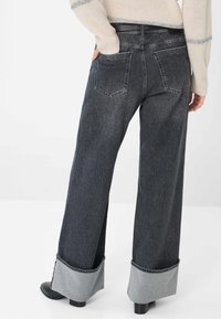 Jeans a gamba larga in denim scuro, con un risvolto in denim chiaro a contrasto e tasche posteriori. Il tessuto ha una texture sottile.