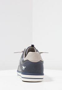 Granatowo-szary sneaker z teksturowanym materiałem i jasnoszarym akcentem na pięcie. Posiada białe logo oraz kontrastującą białą i niebieską podeszwę.