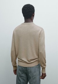 Beige sweater with a round neck, ribbed cuffs, and hem, made of knit fabric. Worn with light gray, high-waisted jeans.