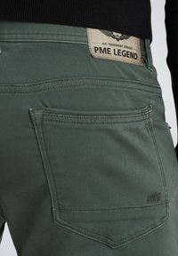 Pantalones de algodón verde oscuro con un diseño destacado de bolsillo trasero, una etiqueta de marca etiquetada "PME Legend" y detalles de costura sutiles.