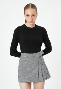 Czarny prążkowany sweter z długim rękawem w połączeniu z mini spódnicą w szachownicę w czarno-białym kolorze, która ma fason typu wrap oraz plisowane detale.