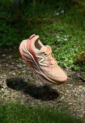 Beige athletic shoe with mesh upper, pink accents, and a textured sole. Features a logo on the side and a heel pull tab for easy wear.