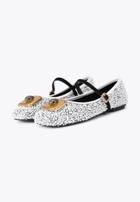 Ballerines plates avec un extérieur couvert de sequins argentés, des lanières noires, des accessoires dorés et un détail unique en forme d'œil sur le bout.
