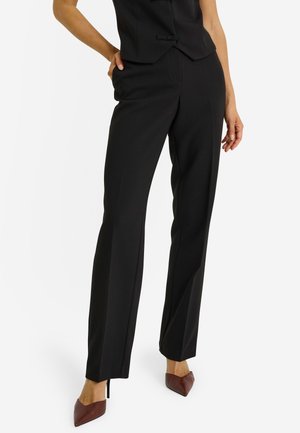 Pantalones negros a medida con diseño de corte recto, con una textura suave y detalles mínimos. Combinados con zapatos de tacón puntiagudos marrones.