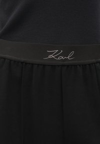 Fekete pliszírozott szoknya sima derékkal, amelyen hímzett "Karl" felirat található. Puha szövet jellemzi, egyszerű és elegáns dizájnnal.