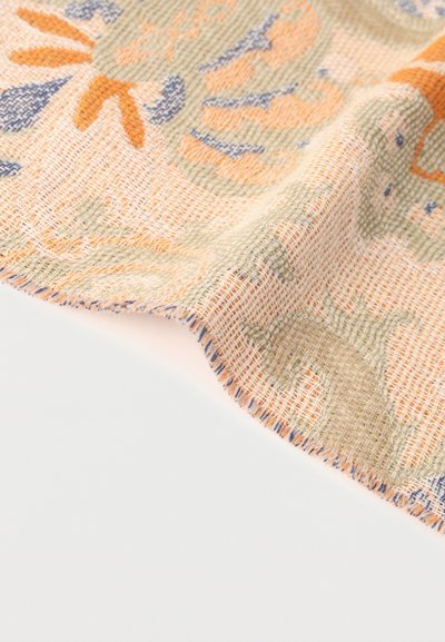 Gros plan sur un tissu à tissage lâche avec des formes abstraites orange, bleues et vertes sur un fond beige, légèrement plié.