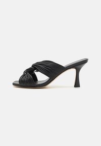 Sandale à talons hauts noire avec un design plissé torsadé, orteils ouverts et un talon stiletto effilé. Texture en cuir lisse.