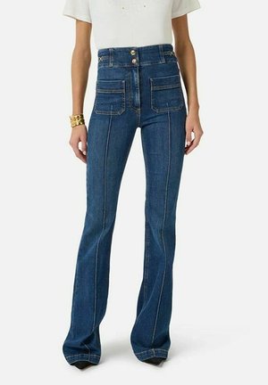 Donna che indossa jeans a gamba larga, vita alta, di colore blu scuro con tasche frontali applicate e chiusura con doppio bottone, abbinati a una maglietta bianca a maniche corte.