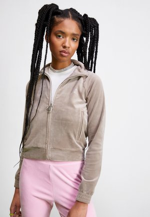 Giacca corta grigia chiara con zip in morbido velluto, dotata di tasche laterali, polsini a costine e zip argentata. Abbinata a pantaloni rosa.
