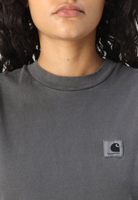 Maglietta grigia a maniche corte con scollatura rotonda e una piccola etichetta nera sul lato sinistro del petto. Tessuto dalla texture liscia, design informale.